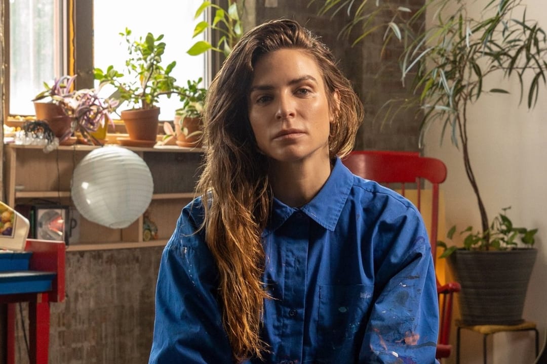 Annina Roescheisen in a paint-flecked blue shirt in her studio, plants in the window behind