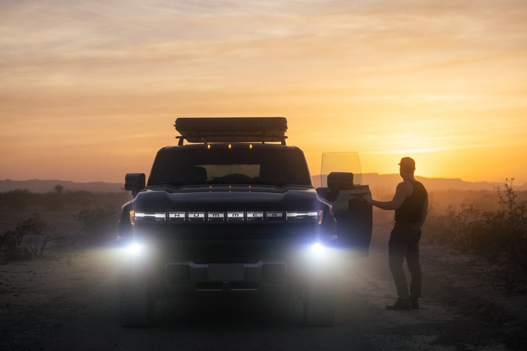 GMC Hummer EV with headlights on at sunset, a man at the open door