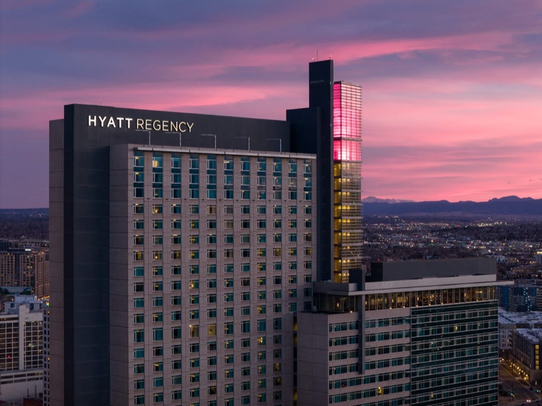 Hyatt Regency Denver at sunset, pink sky over the city and the Rockies on the horizon