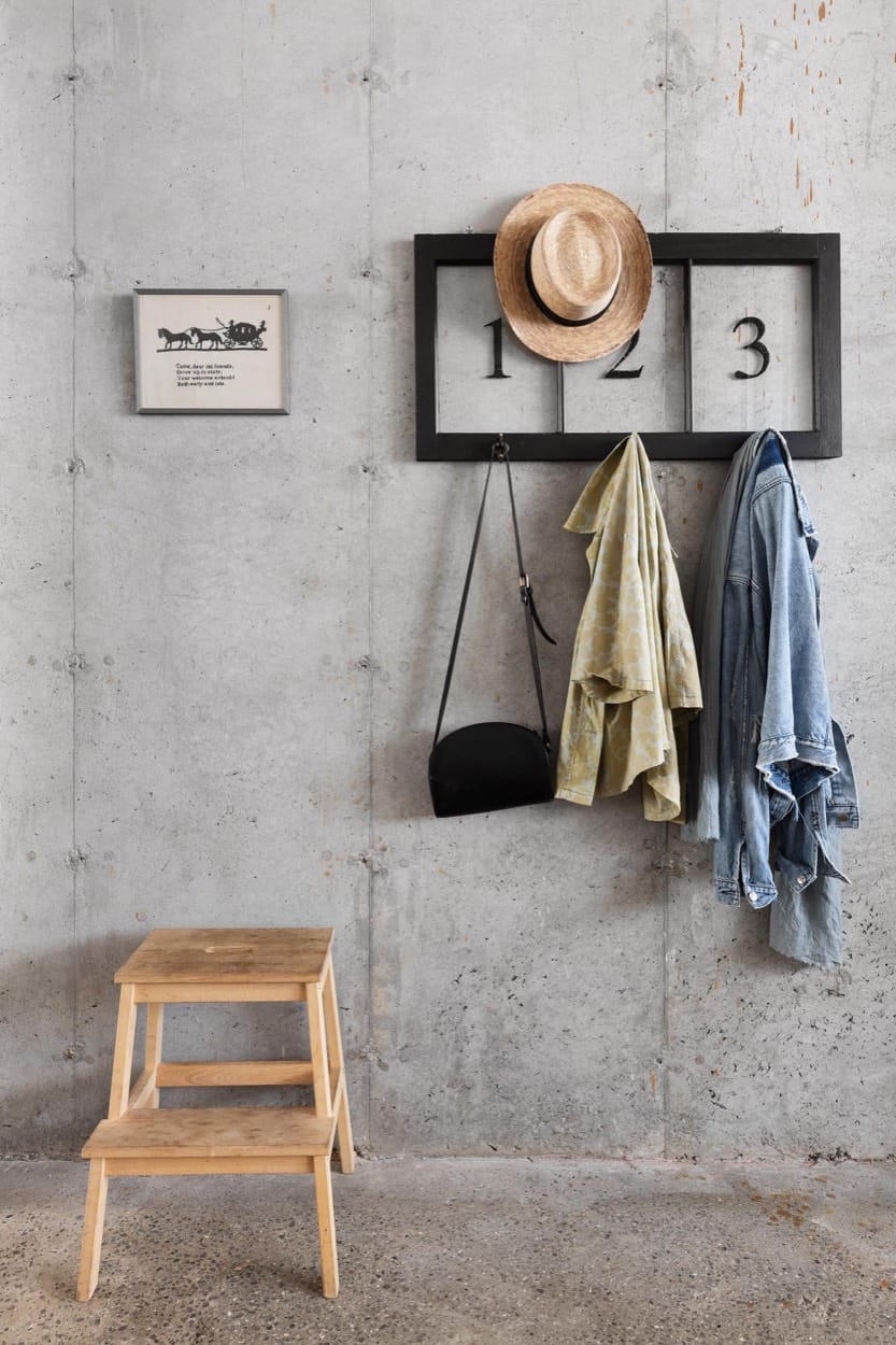 Concrete wall with numbered coat hooks, a straw hat, jackets, a black bag and a wooden step stool