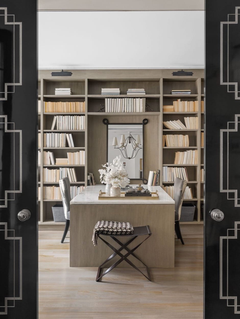 Home library seen through open black doors, a desk and stool before full bookshelves