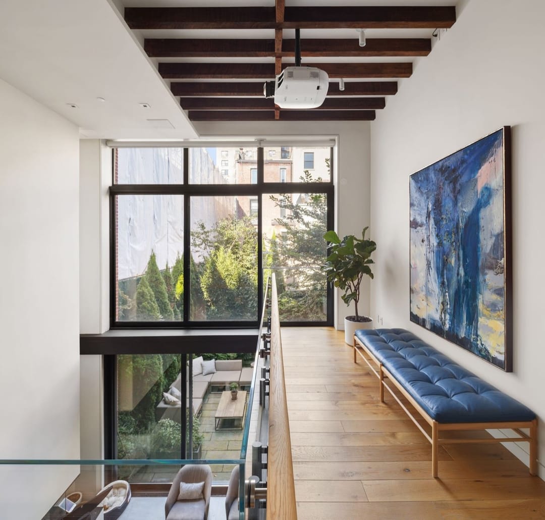 Loft with a mezzanine, dark wood beams, a blue bench and a large abstract painting
