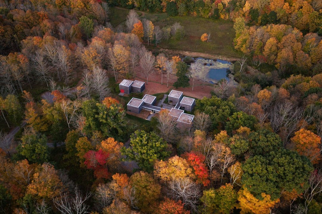 Modern house of weathered wood cubes from above, deep in fall woods beside a pond