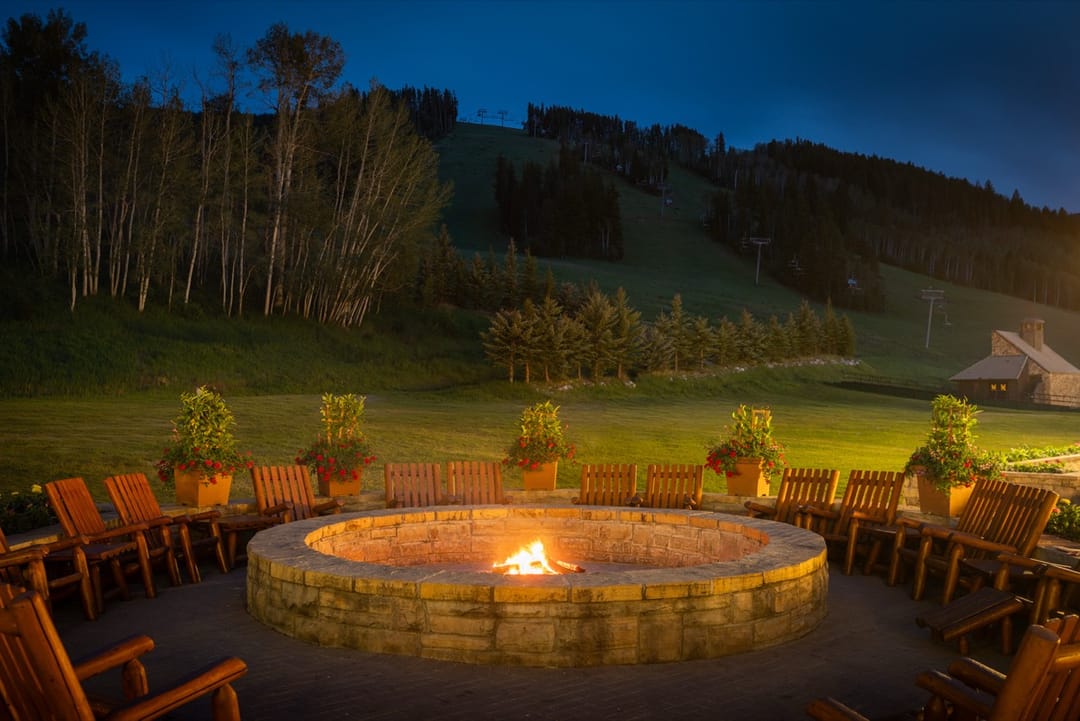 Stone fire pit ringed by wooden chairs at dusk below the ski runs, Park Hyatt Beaver Creek