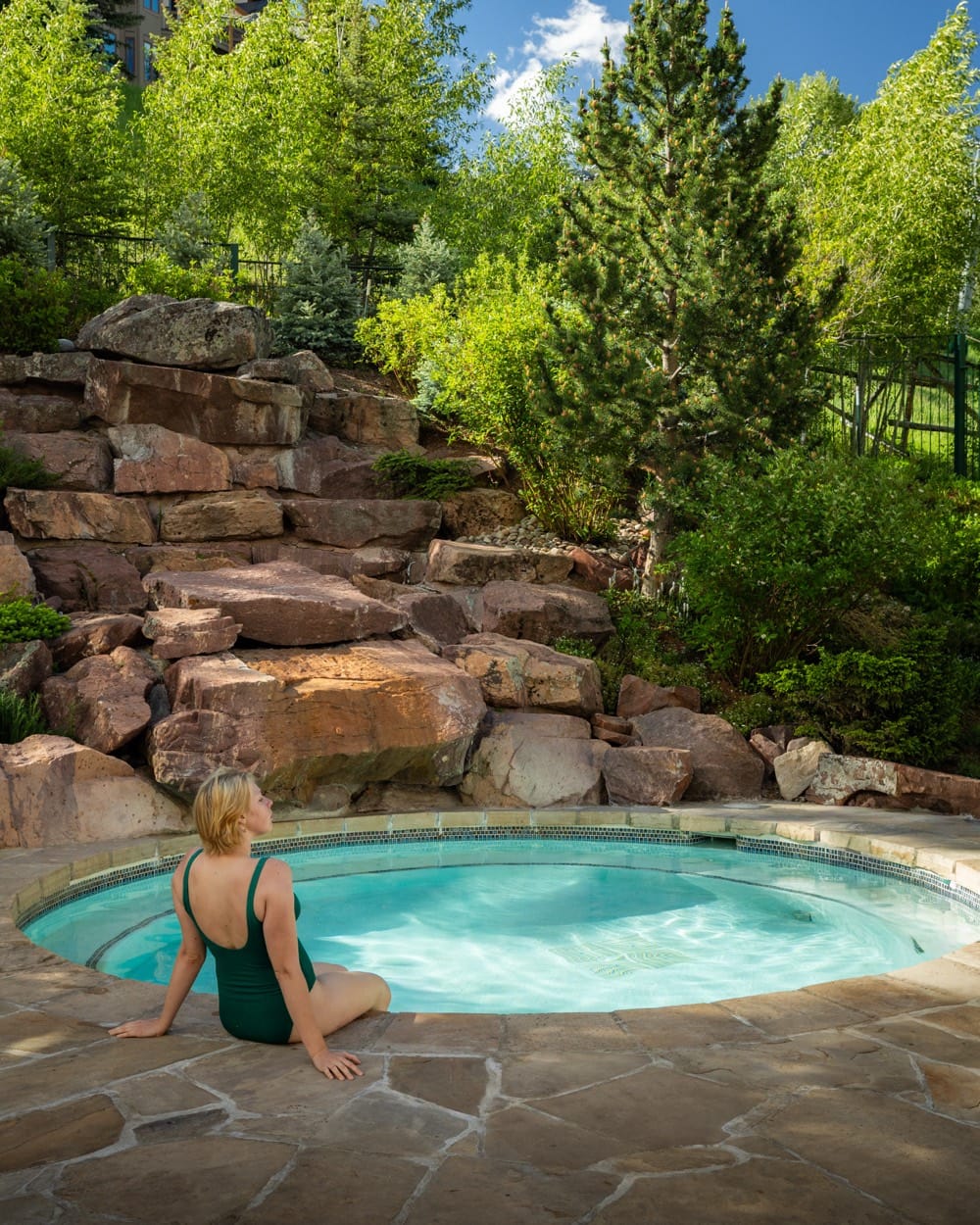 Woman in a green swimsuit at the edge of a hot tub among rocks and aspens, Park Hyatt Beaver Creek