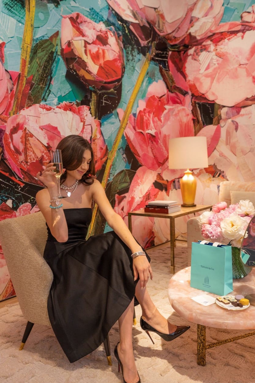 Kate Bartlett with champagne in a room of painted peonies, a Tiffany & Co. bag beside her